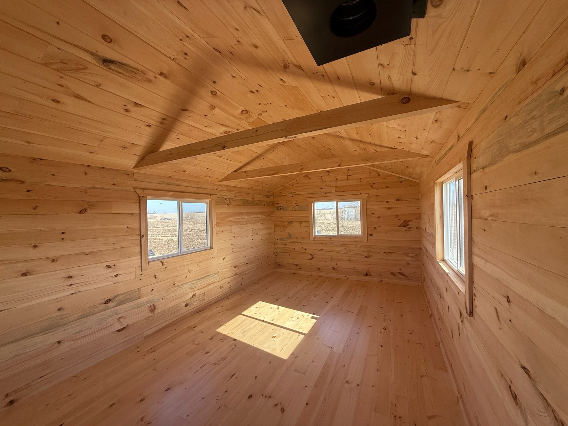 Open cabin interior with exposed beam, dual windows, and stove pipe